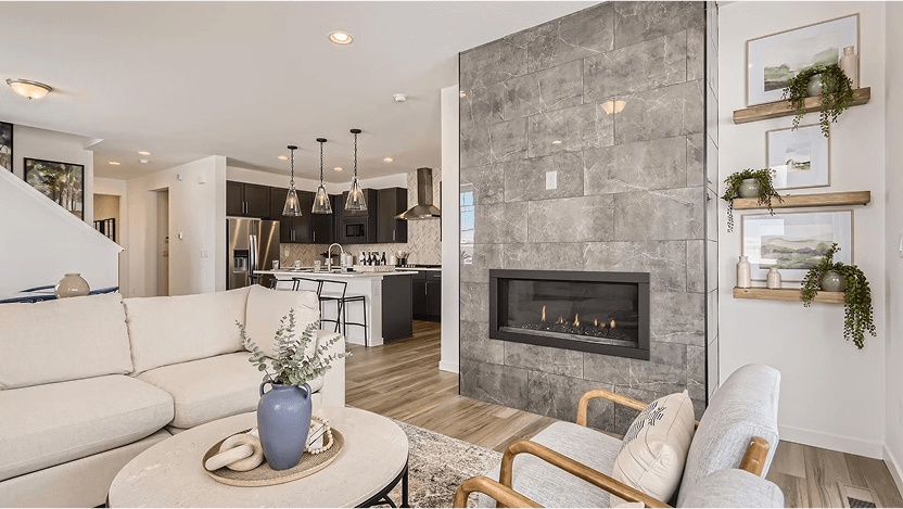 A modern living room with a beige sectional sofa, armchairs, a round coffee table, gray tile fireplace, and an open kitchen with pendant lighting—perfect for those seeking Uplands Westminster homes for sale.