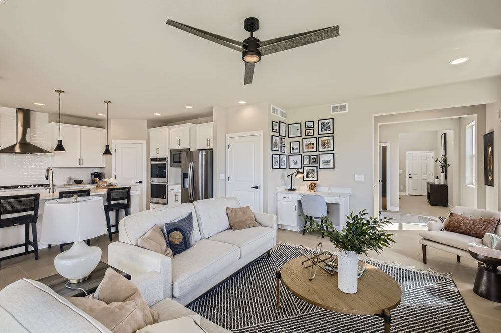 Modern open-concept living room and kitchen with neutral décor, ceiling fan, framed photo wall, desk workspace, and natural light—perfect for those seeking Uplands Westminster homes for sale.