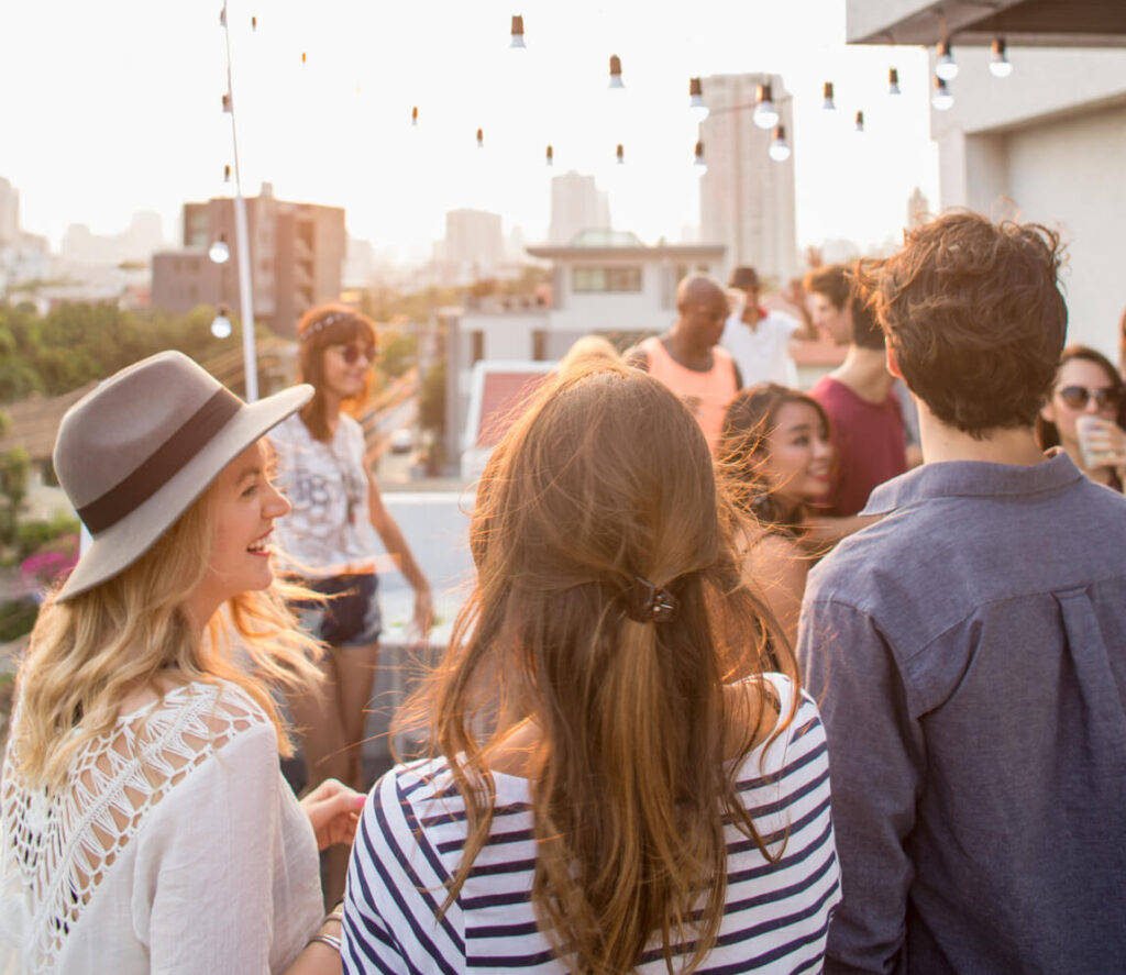 A group of people socializing at a rooftop gathering during the daytime, with city buildings and Uplands Westminster homes for sale in Westminster, CO visible in the background.
