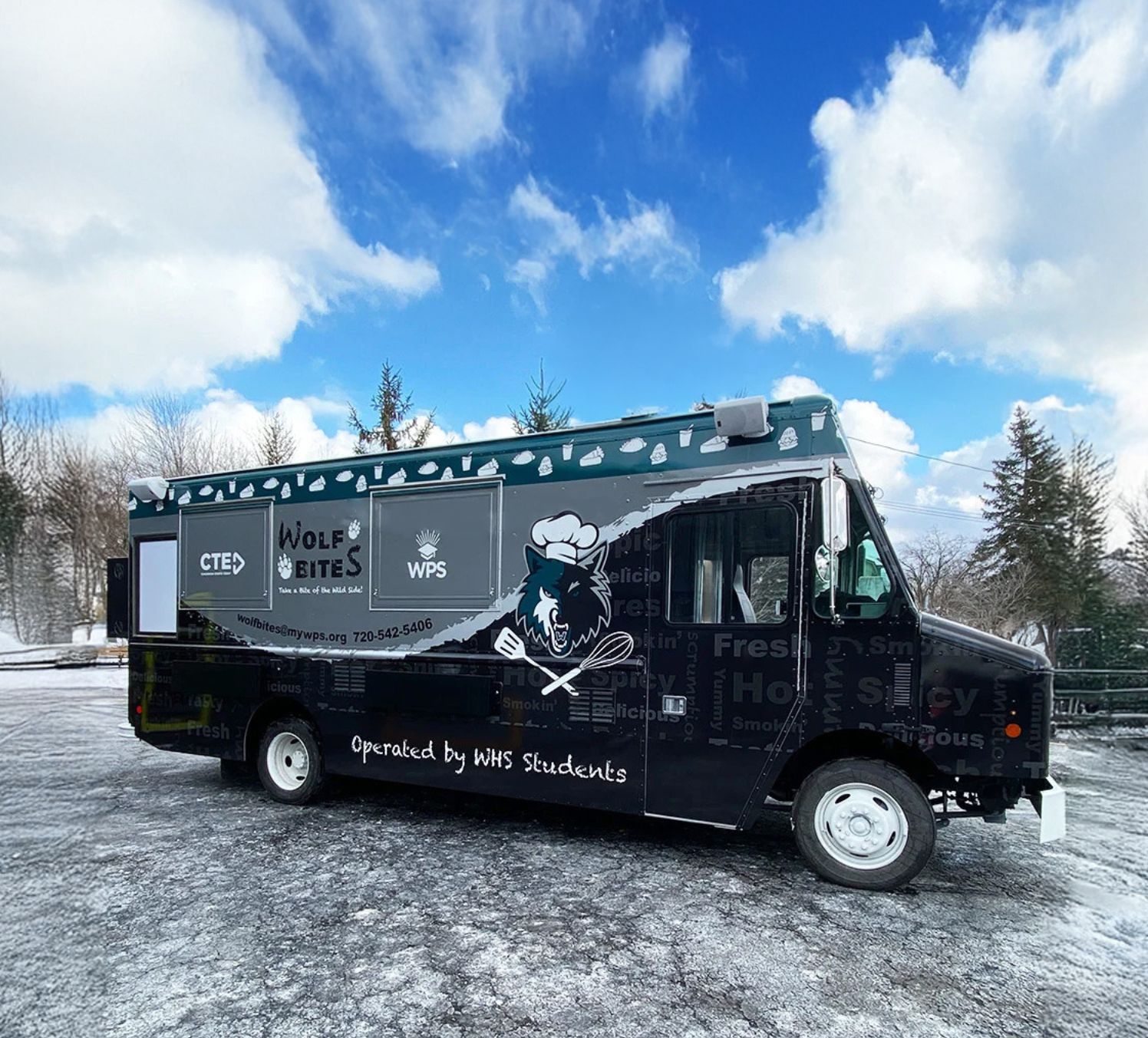 A food truck labeled "Wolf Bites" with a wolf logo is parked on a snowy lot in Uplands Westminster, with trees and a partly cloudy sky in the background.