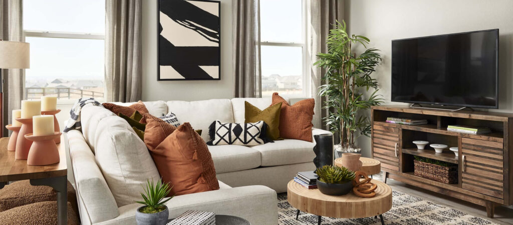 A modern living room in Uplands Westminster features a white sectional sofa, assorted pillows, a wooden coffee table with plants, TV on a console, and abstract wall art, all bathed in natural light—perfect for those seeking Uplands Westminster homes for sale.