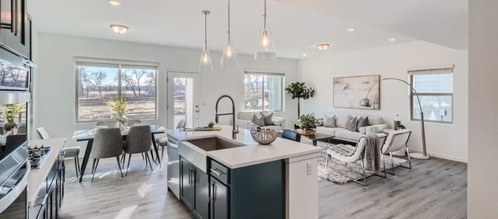 Modern open-concept kitchen and living room with island sink, dining table by large windows, and light wood flooring throughout—discover this inviting space in Uplands Westminster homes for sale.